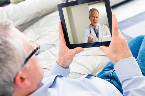 A man holding a tablet, on a video call with a doctor