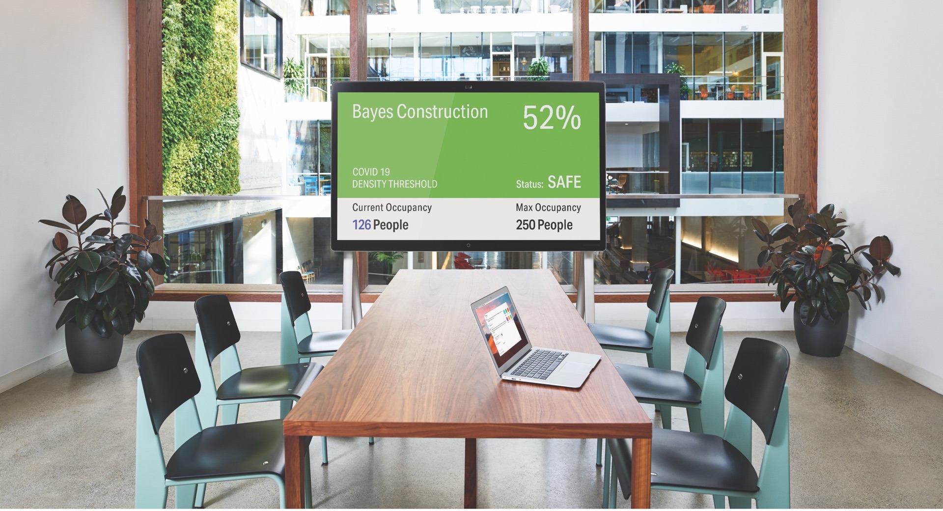 A meeting room with a laptop on a wooden table and a large wall screen showing an occupancy dashboard